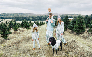 A family of 4 with a dog standing outside in matching pajamas at a Christmas tree farm.