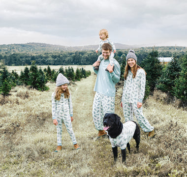 A family of 4 with a dog standing outside in matching pajamas at a Christmas tree farm.